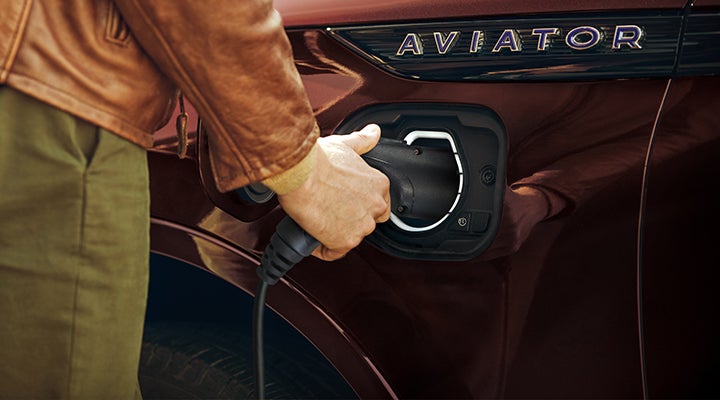 A hand is shown plugging a charger into the charging port of a 2023 Lincoln Aviator® Plug-in Hybrid model. | All Star Lincoln in Prairieville LA