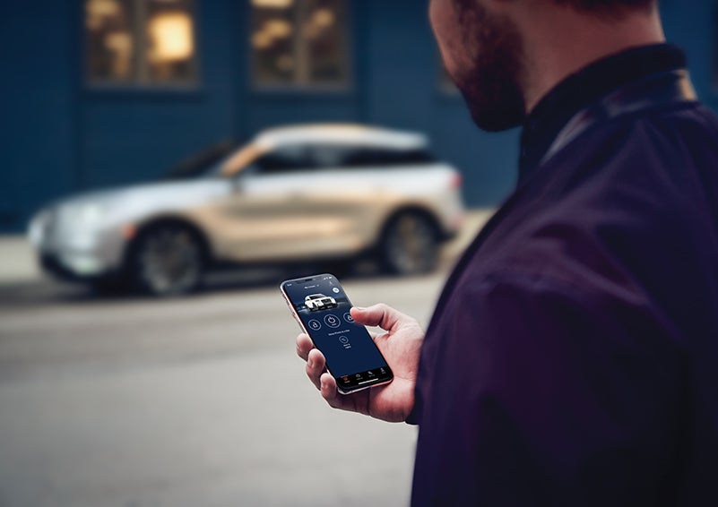 A person is shown interacting with a smartphone to connect to a Lincoln vehicle across the street. | All Star Lincoln in Prairieville LA